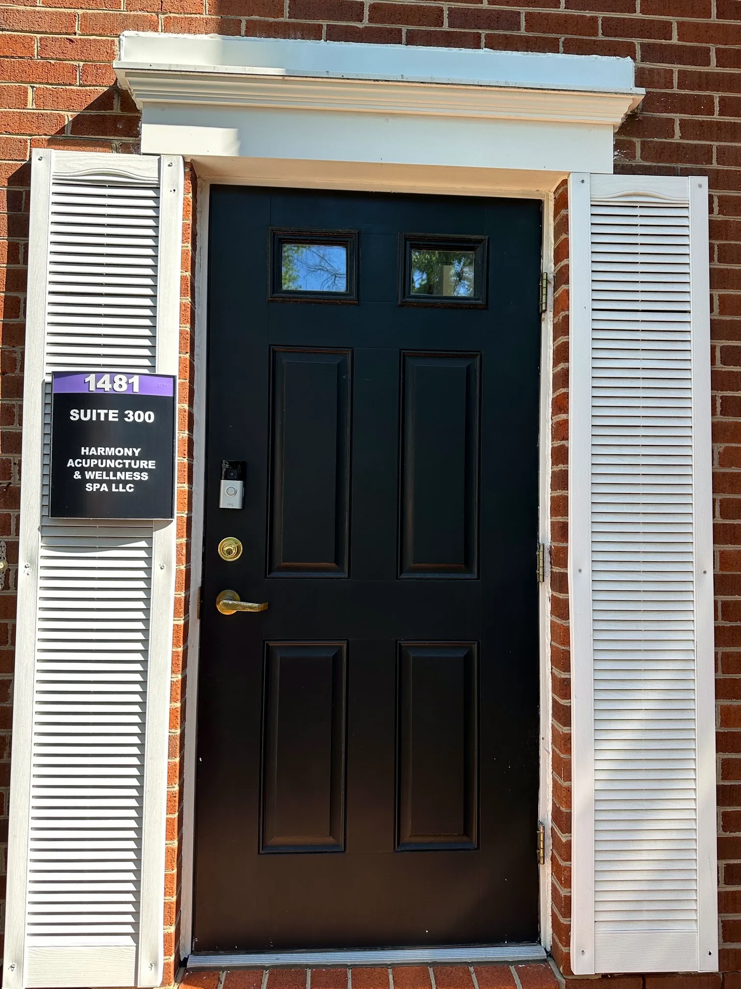 Entrance of Harmony Acupuncture & Wellness Spa: black front door with white shutters on a red brick building, with Ste 300 signage
